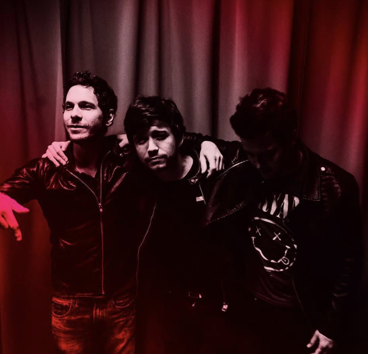 The trio arm-in-arm backstage, red curtains behind