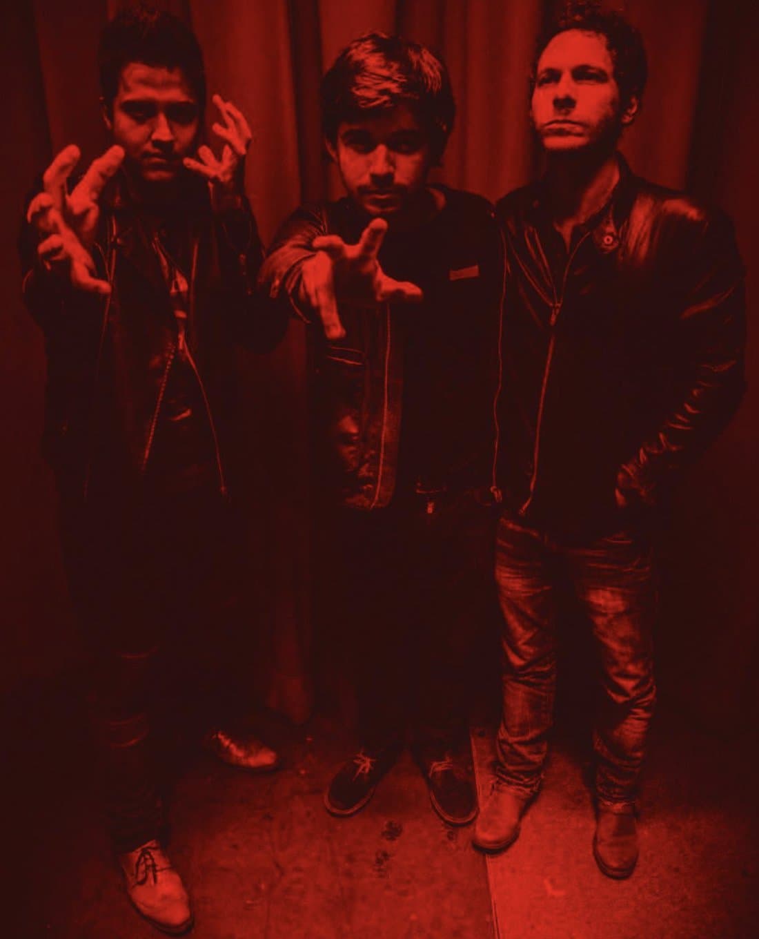 The trio in deep red monochrome, hands reaching toward the camera