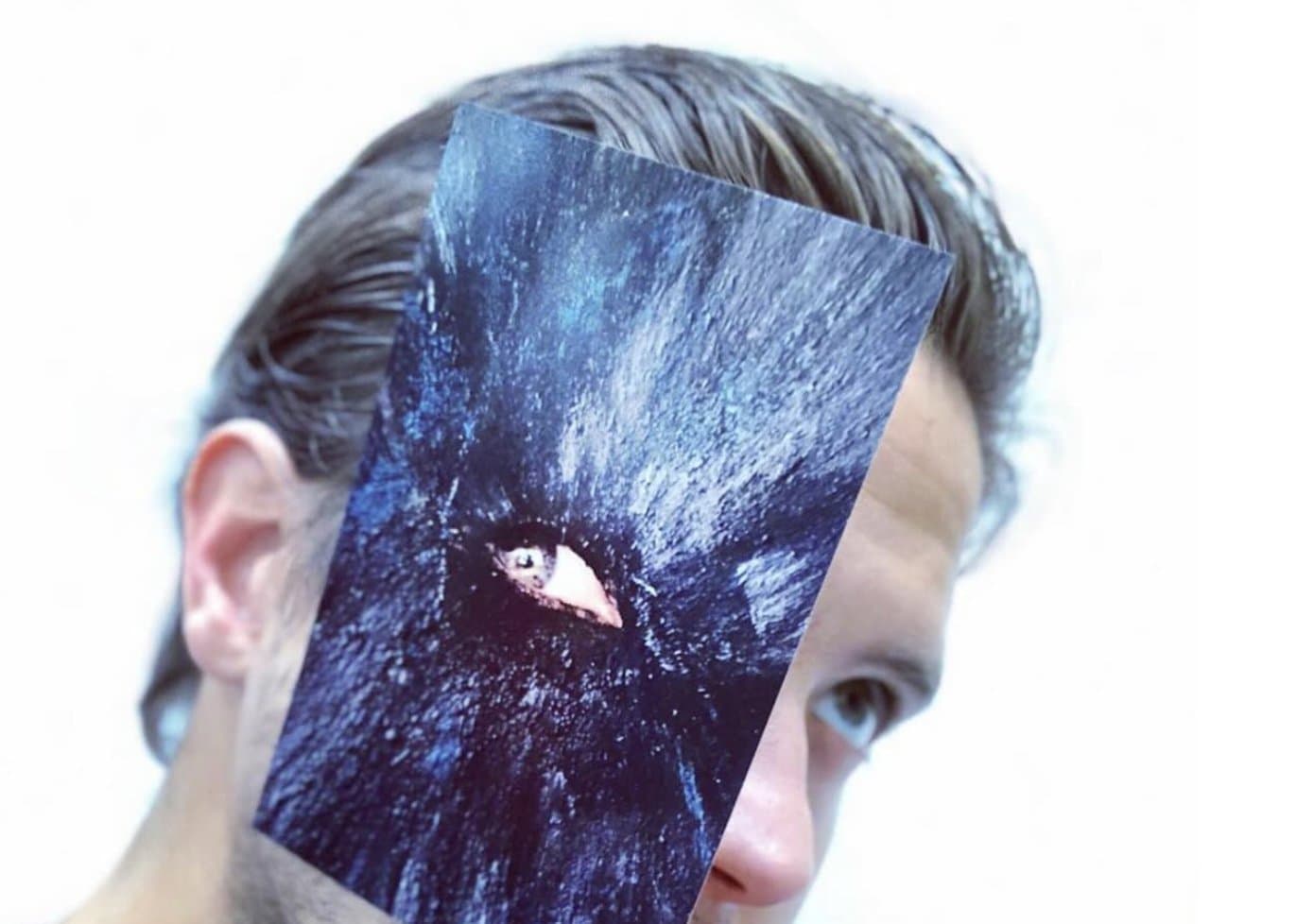 Rodrigo holding a torn dark canvas over his face, a painted eye looking through the hole