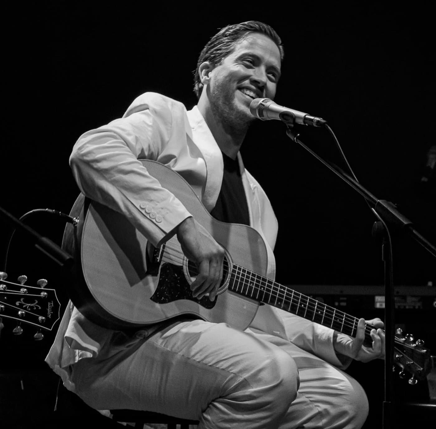 Rodrigo Solo live — white suit, acoustic guitar, black stage