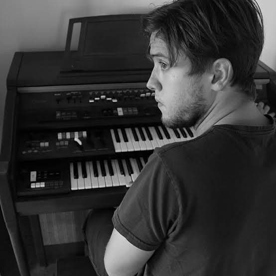 Rodrigo at a vintage organ, looking over his shoulder