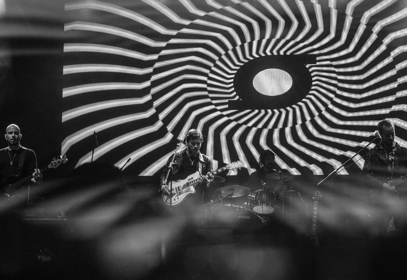 The band on stage under a spiral projection