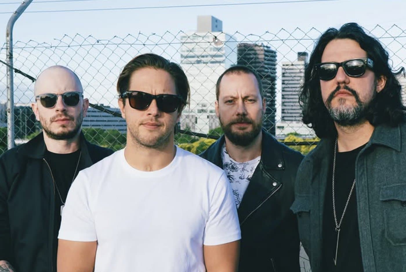The four of Viniloversus against a chain-link fence and the city